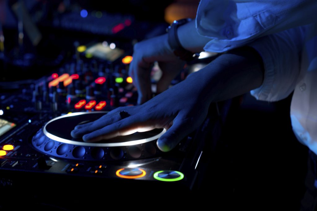 Close up view of the colourful controls on the deck at night with the hands of a DJ mixing and scratching music at a concert using vinyl records on a turntable