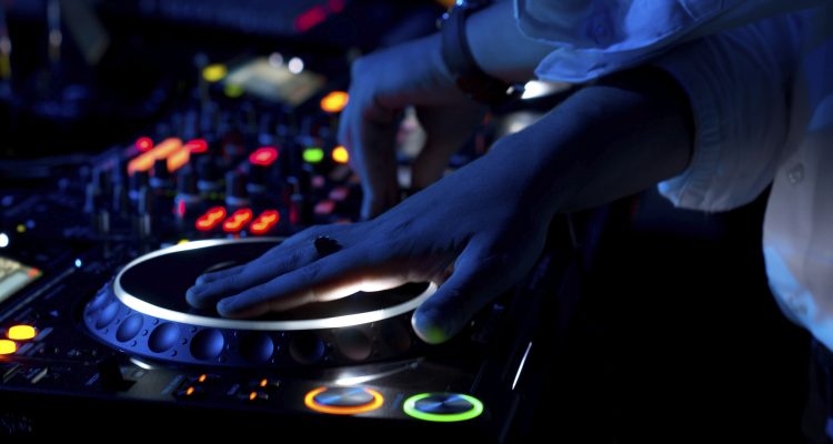 Close up view of the colourful controls on the deck at night with the hands of a DJ mixing and scratching music at a concert using vinyl records on a turntable